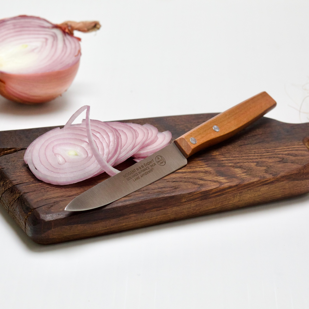 couteau microdentée sur une planche en bois et un oignon rose découpé finement